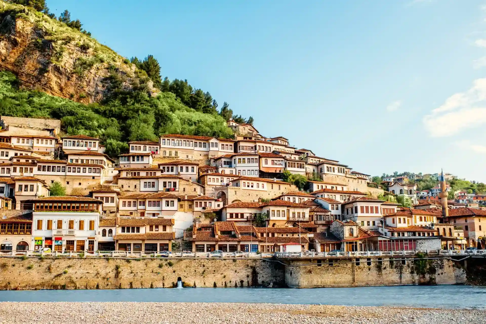 Berat's Mangalem quarter at dusk — Ottoman-era hillside houses with rows of windows facing the Osum river